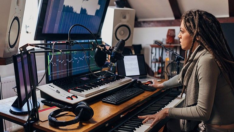 Kvinna med dreadlocks arbetar i en modern hemmastudio eller coworking-miljö för musiker.